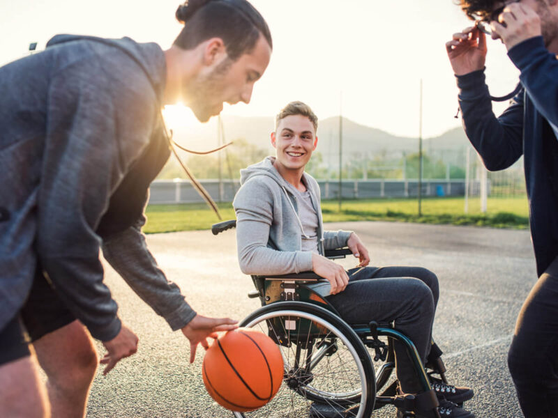 Jugendliche Jungen spielen Basketball im Freien, einer von ihnen im Rollstuhl