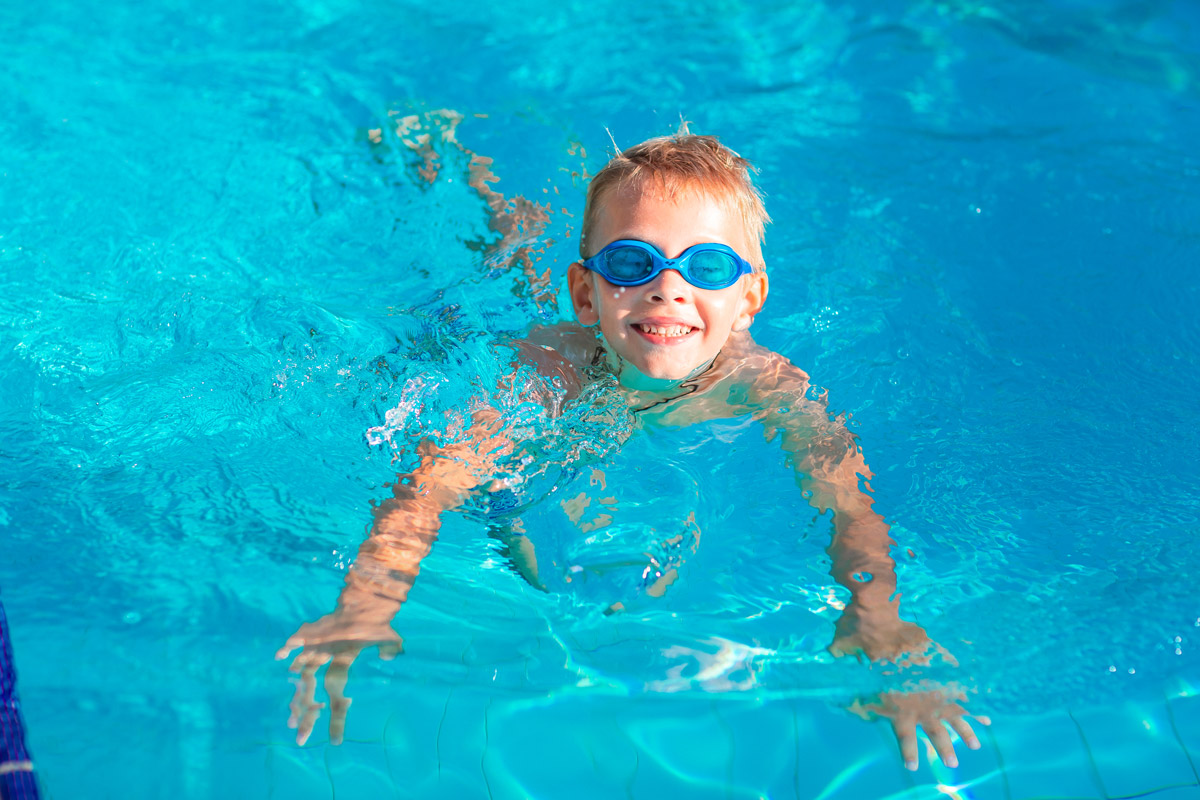 Blonder Junge mit blauer Schwimmbrille im Wasser