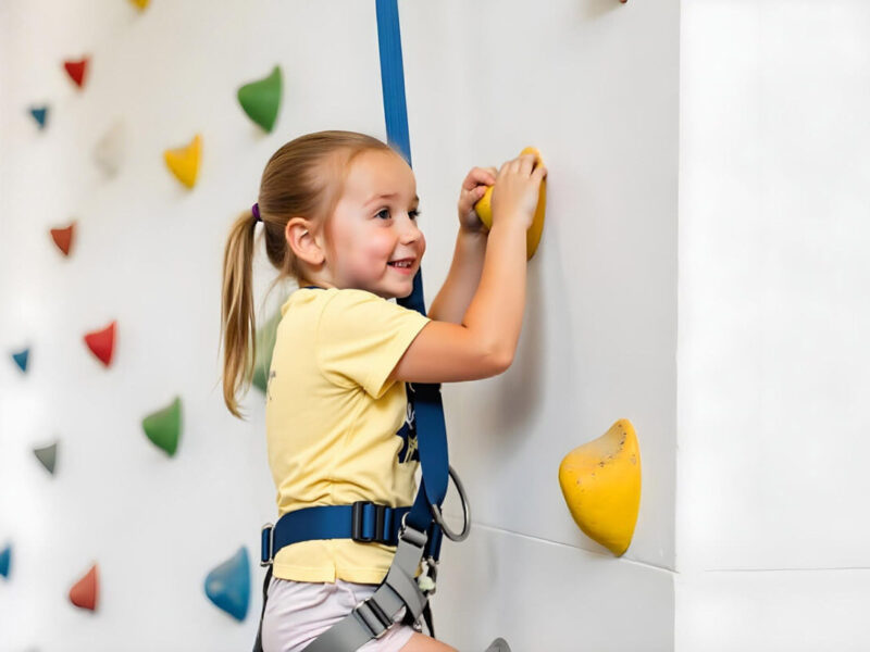 Ein junges, blondes Mädchen an einer Kletterwand